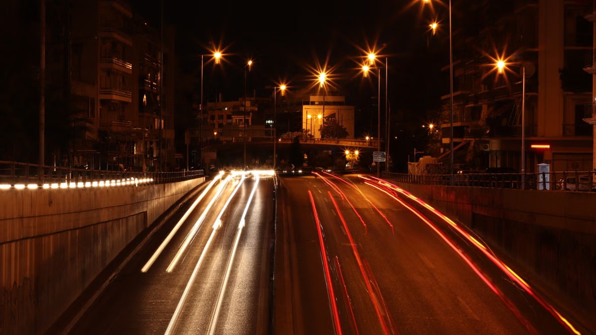 Long exposure of vehicle lights creating trails on a busy Athens road at night.